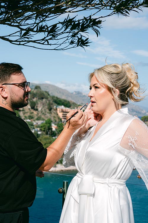 Bride getting makeup done on a terrace overlooking the Mediterranean Sea during her romantic wedding morning in Taormina, Sicily.