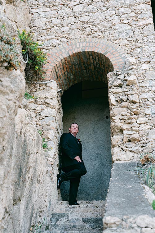 Groom standing under a stone archway carved into the cliffs of Taormina while getting ready for his romantic wedding in Sicily.