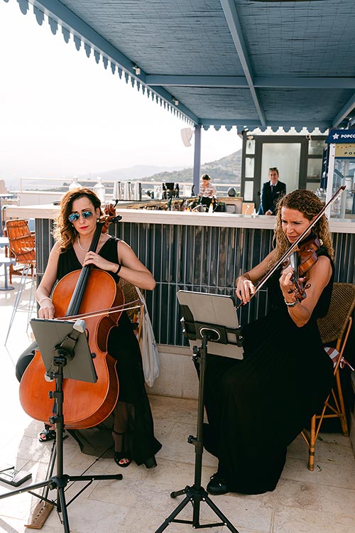 Cellist and violinist performing live music on a panoramic terrace in Taormina during the romantic wedding ceremony in Sicily.
