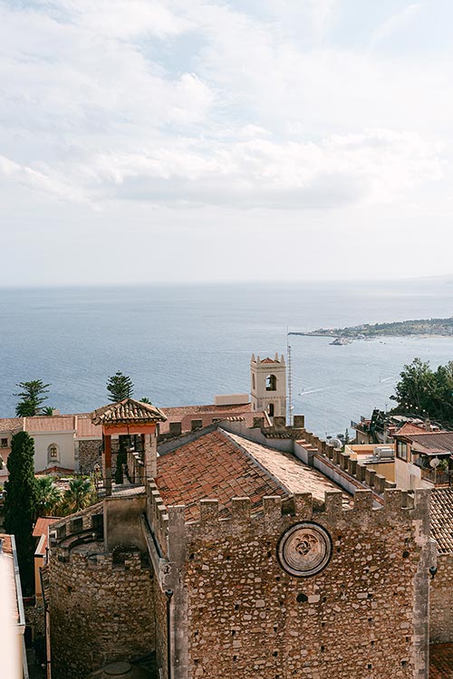 Panoramic view of Taormina’s ancient stone buildings and bell tower overlooking the Mediterranean Sea before the romantic wedding ceremony.