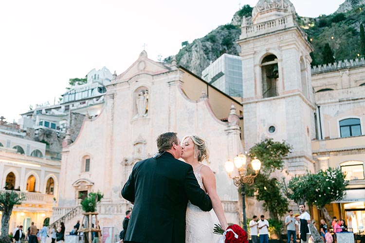 Bride and groom kissing in Piazza IX Aprile in front of the Church of San Giuseppe during their romantic wedding photoshoot in Taormina, Sicily.