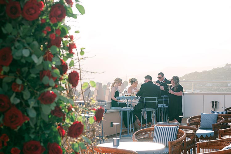 Wedding guests enjoying cocktails on a panoramic terrace in Taormina with red rose décor during the romantic wedding celebration in Sicily.