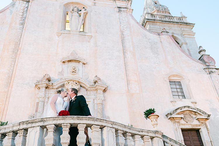 Bride and groom kissing on the stone staircase of the Church of San Giuseppe during their romantic wedding photoshoot in Taormina, Sicily.