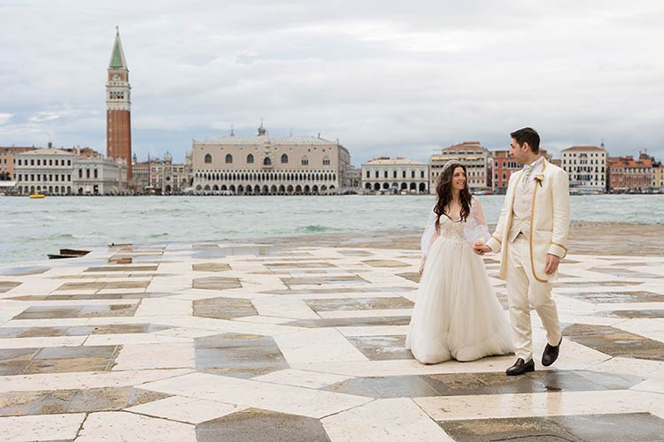 Bride and groom walking along the waterfront in Venice with St. Mark’s Square in the background
