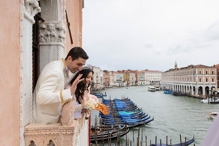 Bride and groom waving from a historic balcony overlooking gondolas on the Grand Canal in Venice