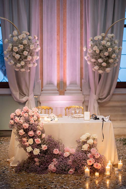 Elegant wedding dinner setup inside a historic Venetian palace with floral centerpieces and warm lighting.
