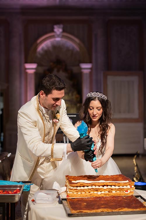 Bride and groom helping the baker prepare their wedding cake during a live show-cooking in a Venetian palace.