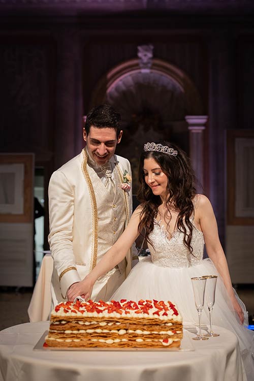 Bride and groom helping the baker prepare their wedding cake during a live show-cooking in a Venetian palace.