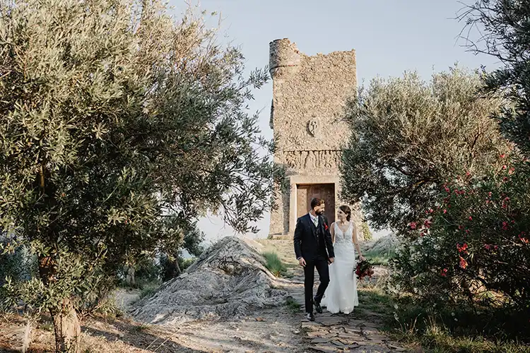 Bride and groom walking among olive trees near an ancient stone tower on the Italian Riviera