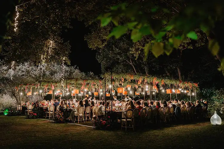 Guests enjoying an elegant outdoor wedding dinner beneath illuminated trees in Liguria